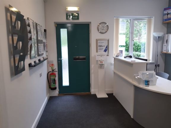 The clinic reception, with a green door, a reception desk and a leaflet stand