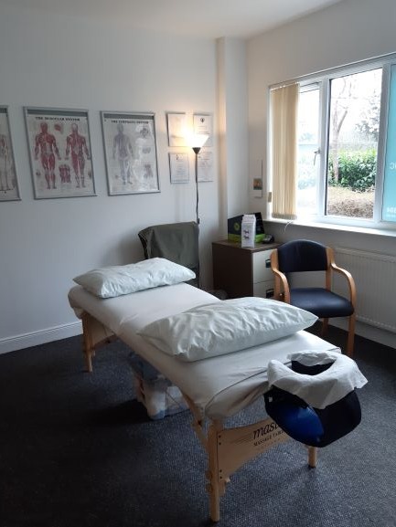 Linda's treatment room: a massage couch with pillows and a face cradle, anatomy charts and framed certificates on the wall